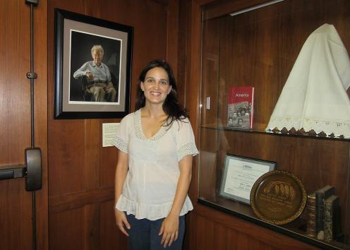 woman in white shirt standing in front of wood paneled wall with a framed photo on her right and gallery display on her left
